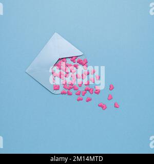 Ein Liebesbrief mit pinkfarbenen Papierherzen auf blauem Hintergrund mit Kopierbereich – Valentinstag-Grußkartendesign Stockfoto