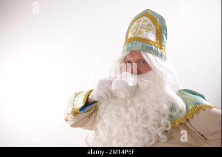 Sinterklaas-Porträt. USA auf weißem Hintergrund. Holländischer Weihnachtsmann St. Nikolaus weihnachten Neujahr Foto des Ruheständlers positiver Mann Hold Becher köstliches leckeres Getränk Eierpunsch heißer Schokoladentee Stockfoto
