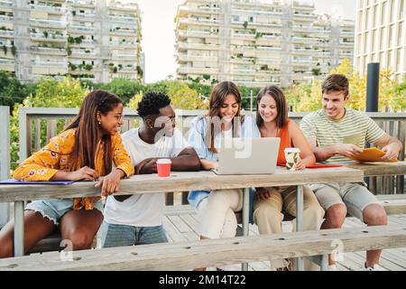 Lächelnde multirassische Studenten, die im Internet suchen und lustige Videos auf dem Universitätscampus ansehen. Fröhliche und positive Gruppe junger Freunde, die im Freien lachen und Inhalte in den sozialen Medien teilen. Bildungskonzept. Hochwertiges Foto Stockfoto