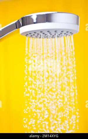 Nahaufnahme fließender Wassertropfen aus einem Duschkopf in einem hellen Badezimmer mit gelbem Hintergrund Stockfoto