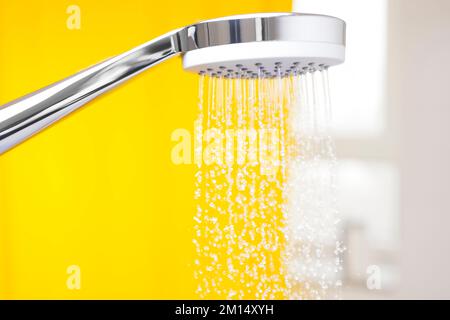 Nahaufnahme fließender Wassertropfen aus einem Duschkopf in einem hellen Badezimmer mit gelbem Hintergrund Stockfoto