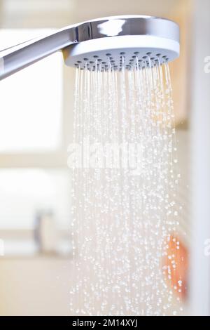 Nahaufnahme von fließenden Wassertropfen aus einem Duschkopf in einem hellen Badezimmer mit Fenster im Hintergrund Stockfoto