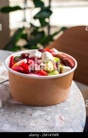 Griechischer Diät-Salat mit Feta, Tomaten, Grün auf grauem Steinhintergrund. Konzeptessen Für Partys. Fast Food. Gesundes Mittagessen. Lebensmittellieferung im Entsorgungsraum Stockfoto