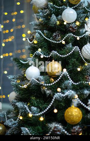 Weiße und goldene Kugeln, Perlen, leuchtende Girlande auf dem Weihnachtsbaum. Stockfoto