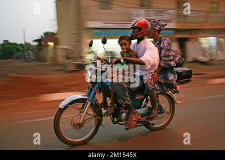 Ein Mann fährt mit seinem Kind und seiner Frau auf den Straßen von Malis Hauptstadt Bamako mit dem Motorrad. Stockfoto