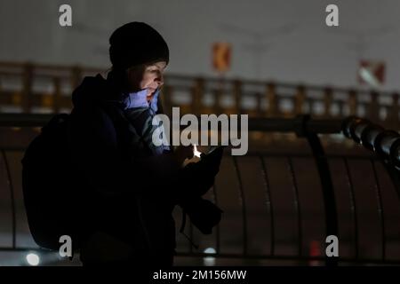 Frauen in Winterkleidung auf der dunklen Straße sehen in ihrem Handy mit Licht aus dem Bildschirm aus Stockfoto