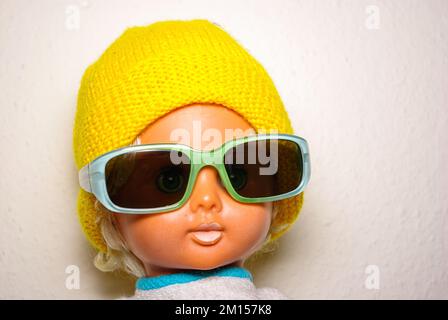 Schicke Puppe mit Sonnenbrille und gelber Strickmütze, Kinderspielzeug aus der DDR der 1970er, Konzept des kindlichen Spielens und des menschlichen Ausdrucks. Stockfoto