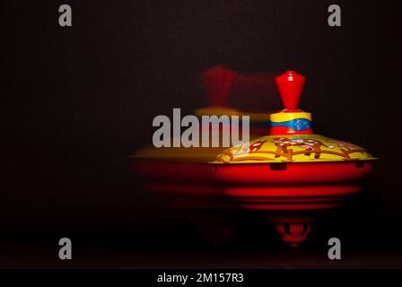 Das sich drehende und sich bewegende, summende Oberteil vor schwarzem Hintergrund, das Konzept des Spielens für Kleinkinder und Spielzeuge. Stockfoto