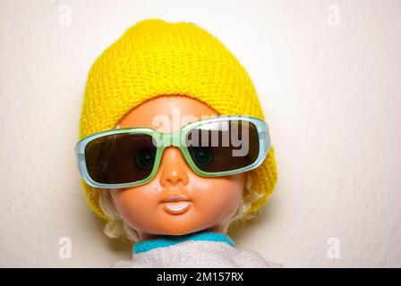 Schicke Puppe mit Sonnenbrille und gelber Strickmütze, Kinderspielzeug aus der DDR der 1970er, Konzept des kindlichen Spielens und des menschlichen Ausdrucks. Stockfoto