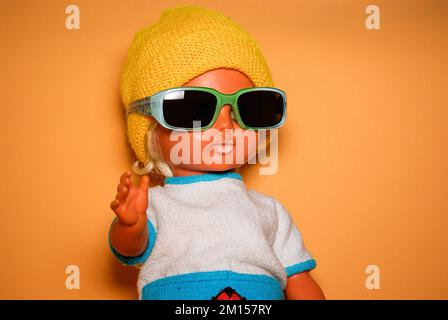 Schicke Puppe mit Sonnenbrille und gelber Strickmütze, Kinderspielzeug aus der DDR der 1970er, Konzept des kindlichen Spielens und des menschlichen Ausdrucks. Stockfoto