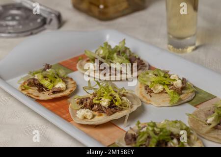 Nahaufnahme von Chalupas, typisches mexikanisches Gericht mit Tortillas, Sauce, Käse, Fleisch und Salat. Stockfoto