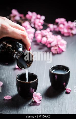 Ungefilterter japanischer Sake mit blühenden rosa Blumen. Sake in Keramik serviert. Stockfoto