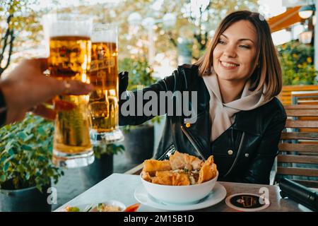Glückliche Frau, die mit einem Mann in einem asiatischen Café in Deutschland Bier trinkt. Positive Dame bei der oktoberfestfeier. Stockfoto