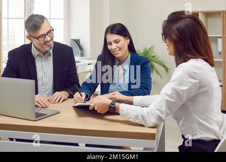 Glückliches Paar, das Kunden der Bank ist, unterzeichnet Papierdokument, das den Kredit für den Kauf eines Hauses bestätigt. Stockfoto