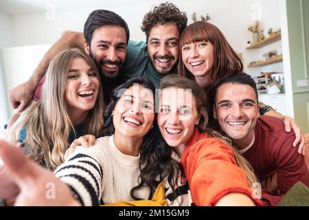 Eine große Gruppe weißer Freunde, die Selfie machen und im Wohnzimmer einer modernen Jugendherberge sitzen Stockfoto