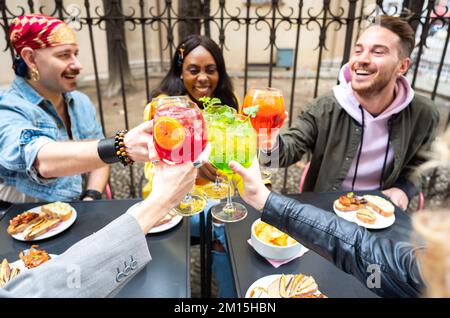 Multikulturelle Freunde stoßen mit farbigen Cocktails an der Bar im Stadtzentrum an Stockfoto