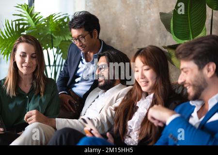 Firmenporträt von Geschäftsleuten, die sich auf der Couch entspannen - multiethnisches Business-Team, das Videos auf dem Smartphone ansieht Stockfoto