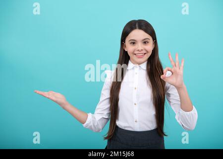 Positive Teenager Kind zeigt sich mit fröhlichem Ausdruck beiseite, zeigt erstaunlich auf leeren leeren Raum. Werbung und Mockup. Stockfoto