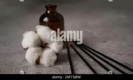 Aroma-Diffusor mit Baumwolle. Aromatherapie auf dunklem Marmorhintergrund. Stöcke und Glasflasche mit Baumwollblume Stockfoto