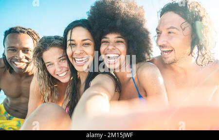 Wunderschöne junge brasilianische Frau lächelt und macht Selfie, wenn sie zusammen mit seinen Freunden in die Kamera schaut - eine Gruppe von Freunden, die aus mehreren Rassen stammen und sich am Abend entspannen Stockfoto