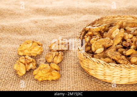 Ein paar geschälte Walnüsse in einem Strohteller auf einem Jutetuch, Makro. Stockfoto