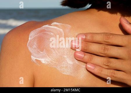 Hand verteilt liebevoll Hautschutz Sonnencreme auf dem Rücken des Mädchens Stockfoto