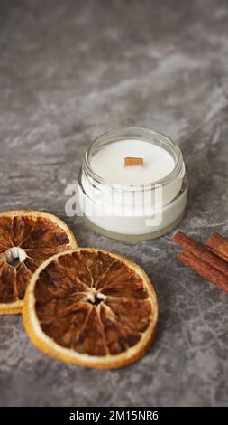 Aroma-Kerze in einem Glasgefäß. Das Aroma von Zimtstäbchen, Zitrusfrüchten. Vertikales Foto auf Marmorhintergrund Stockfoto