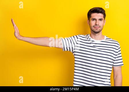 Portrait eines selbstbewussten, ruhigen jungen Mannes Handfläche zeigen einen leeren Raum mit unterdrückter Geste auf gelbem Hintergrund Stockfoto