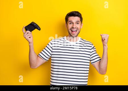 Porträt eines überglücklich erfreulichen Mannes Hold Gamepad hebt die Faust auf gelbem Hintergrund hervor Stockfoto