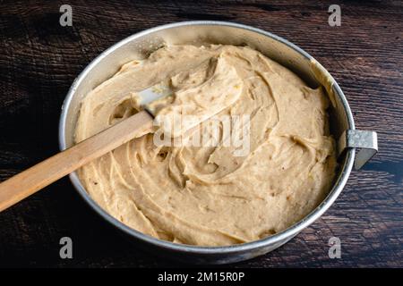 Würziger Kuchenteig in einer runden Kuchenpfanne mit Teigschaber: Dicker Kuchenteig in einer kreisförmigen Kuchenpfanne aus Metall mit einem Silikonspachtel Stockfoto