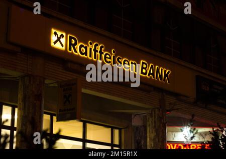 Bukarest, Rumänien - 10. Dezember 2022: Schild und Logo der österreichischen Bank Raiffeisenbank Bank am Abend auf der Straße in Bukarest Stockfoto