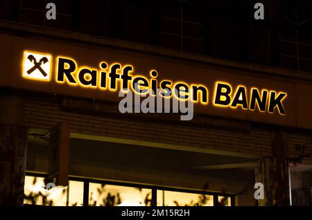 Bukarest, Rumänien - 10. Dezember 2022: Schild und Logo der österreichischen Bank Raiffeisenbank Bank am Abend auf der Straße in Bukarest Stockfoto