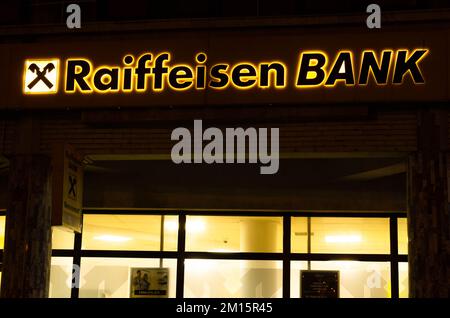 Bukarest, Rumänien - 10. Dezember 2022: Schild und Logo der österreichischen Bank Raiffeisenbank Bank am Abend auf der Straße in Bukarest Stockfoto