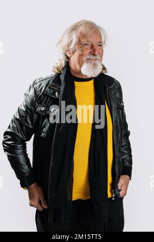 Selbstbewusster, bärtiger Senior-Mann in Lederjacke und Schal, der vor weißem Hintergrund wegschaut Stockfoto