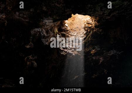 Von unten sehen Sie einsame Sonnenstrahlen, die durch den Abstieg in die steinige Höhle auf Lanzarote scheinen Stockfoto