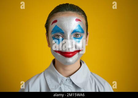 Ein Kind mit grünem Haar und farbenfrohem Make-up in einem weißen Hemd, das auf die Kamera schaut, während er Superschurke mitspielt Stockfoto