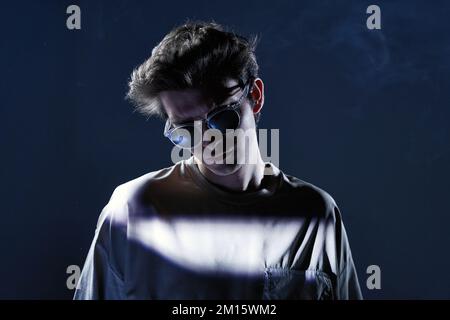 Männliches Model in legerem T-Shirt und Sonnenbrille mit dunklem Haar im Studio mit leuchtendem Licht Stockfoto