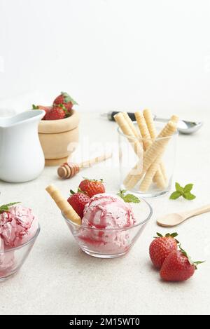 Köstliche hausgemachte Erdbeer-Eislöffel, serviert in einer Glasschüssel mit Beeren und Waffelrolle in der Küche bei Tageslicht Stockfoto