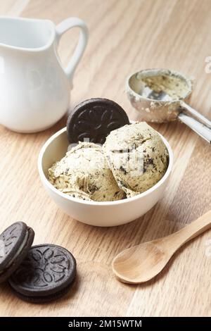 Hausgemachtes Eis mit Schokoladenflocken, serviert in einer Schüssel mit Keksen und auf dem Tisch neben dem Schaufel und dem Krug und dem Löffel in der Küche Stockfoto