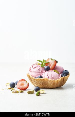 Leckere Eiswürfel auf knusprigen Waffelschüsseln, dekoriert mit frischen reifen Erdbeeren, Blaubeeren, Pistazien und Minzblättern auf weißem Hintergrund Stockfoto