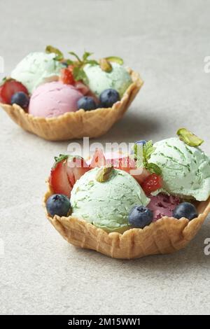 Hausgemachte Pistazien- und Erdbeereisschaufeln, serviert in Waffelschüssel und dekoriert mit frischen Beeren bei Tageslicht Stockfoto