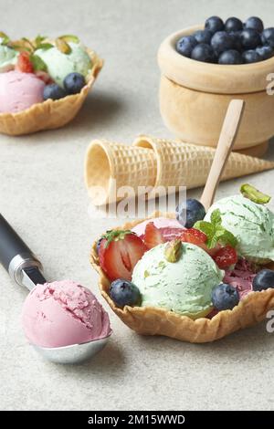 Hausgemachte Pistazien- und Erdbeereisschaufeln, serviert in Waffelschüssel und dekoriert mit frischen Beeren bei Tageslicht Stockfoto