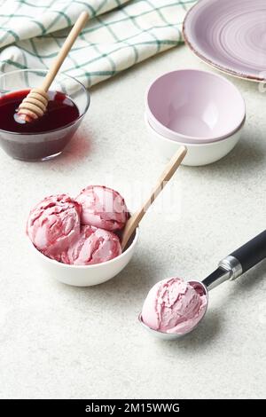 Hausgemachte Eiscreme mit hohem Winkel, serviert in einer Schüssel und garniert mit Beerensirup in einer hellen Küche Stockfoto