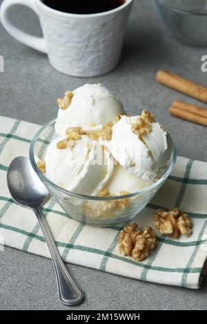 Von oben leckere hausgemachte Eislöffel mit Walnüssen, serviert in einer Glasschüssel auf dem Tisch mit einer Tasse Kaffee und Zimtstangen in der Küche Stockfoto