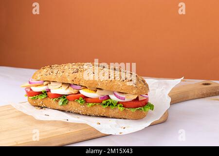 Köstliches Sandwich mit hart gekochtem Ei, frischem Salat, Thunfisch und Tomaten, serviert auf Backpapier auf hackenden Holzbrettern auf farbenfrohem Hintergrund Stockfoto