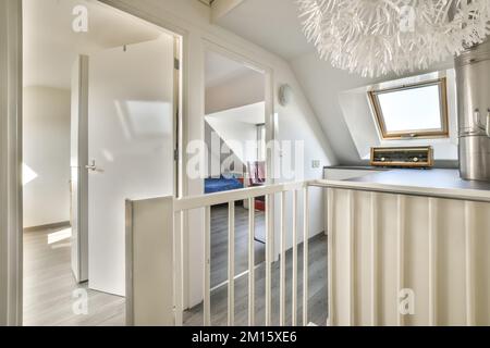 Korridor in Mansarde mit Treppe nach unten und Holzboden im hellen Haus mit weißen Wänden am Tag Stockfoto