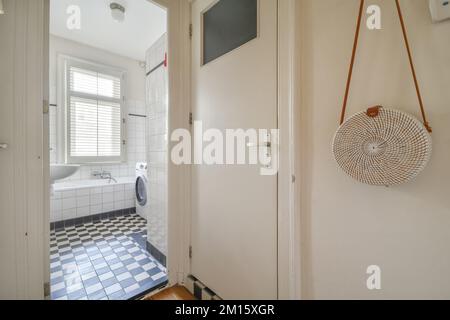 Korridor mit Eingangstür und Parkettboden in zeitgenössischem Apartment in der Nähe des Badezimmers mit weiß gefliesten Wänden in minimalistischem Stil Stockfoto