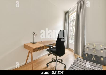 Komfortabler Stuhl am klassischen Holzschreibtisch an der weißen Wand in einem hellen Raum mit rundem Kronleuchter in einem geräumigen Apartment Stockfoto