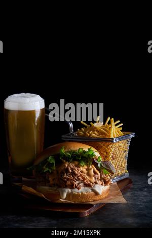 Leckerer Burger mit Schweinefleisch mit Barbecue-Sauce, Cheddar-Käse und Salat, serviert mit Pommes Frites und einem Glas kaltem Bier auf Holzbrett Stockfoto
