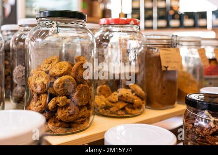 Verschiedene Arten von Keksen und getrockneten Früchten und Gewürzen in Glasgefäßen auf Holzregalen im örtlichen Geschäft Stockfoto